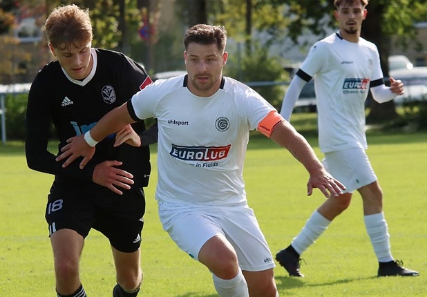 Ein Fußballspieler des VfR Garching trägt ein weißes Trikot mit blau-rotem Eurolub-Logo, während er sich in einem Zweikampf den Ball sichert.